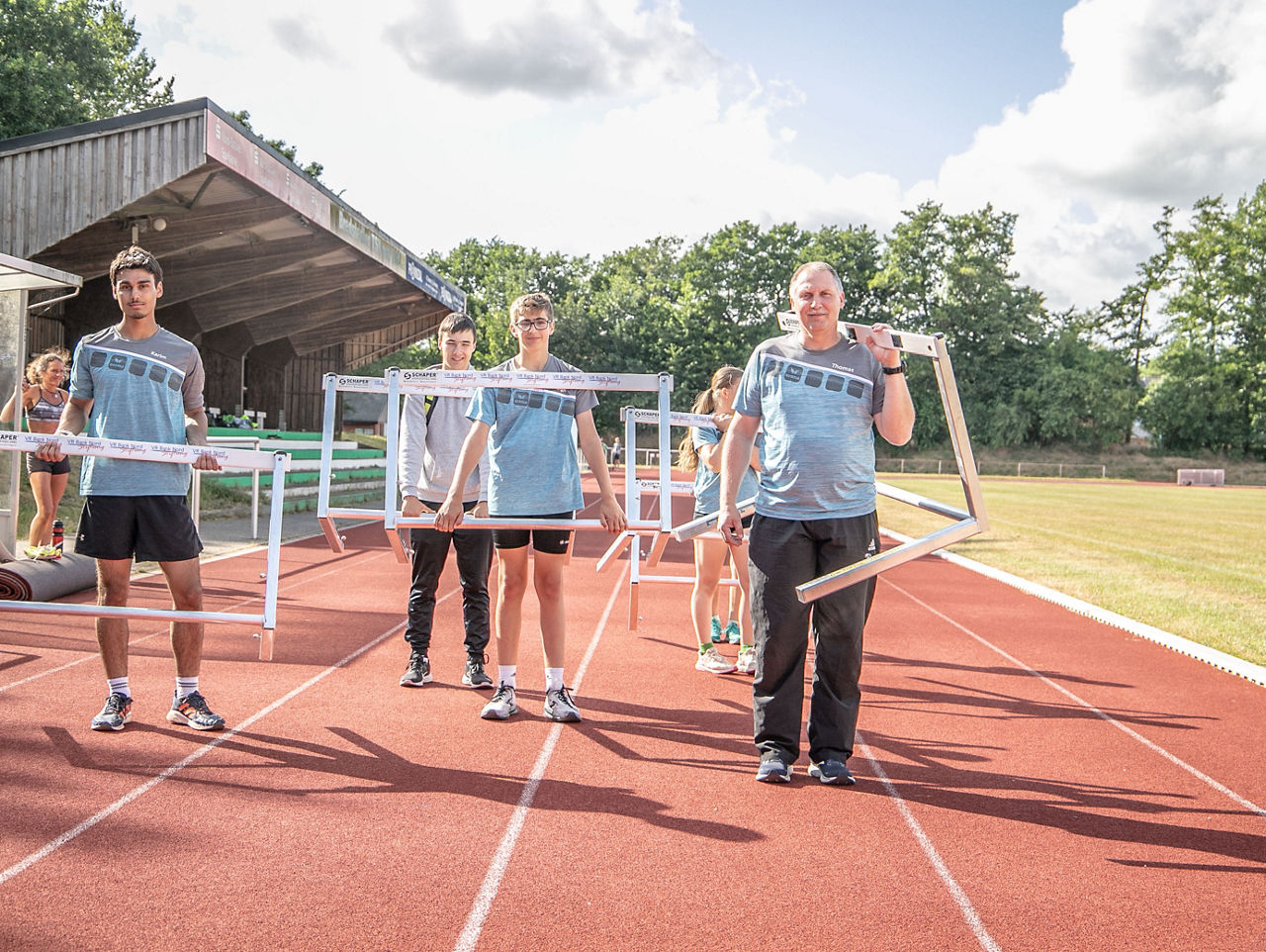 Eine Leichtathletik-Trainingsgruppe trägt Hürden über eine Laufbahn