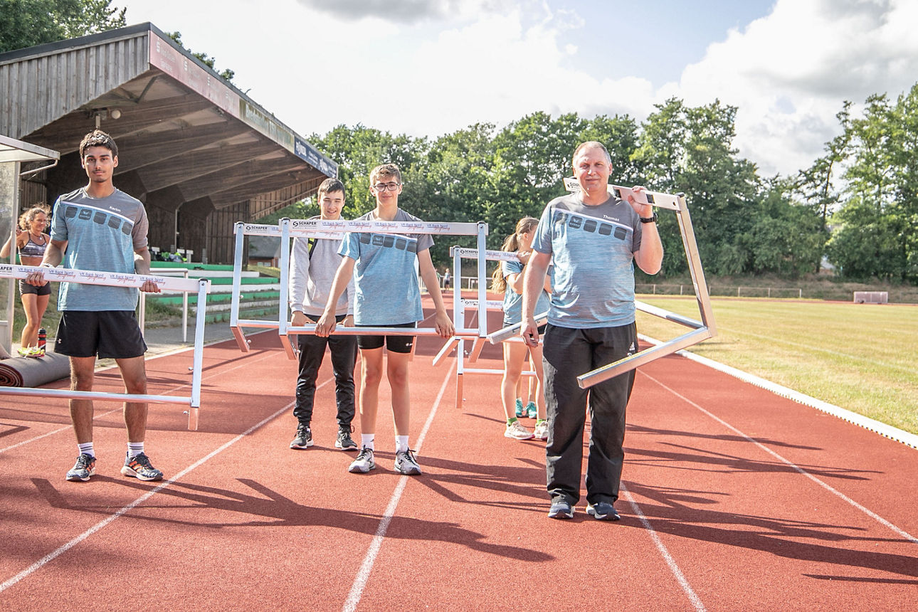 Eine Leichtathletik-Trainingsgruppe trägt Hürden über eine Laufbahn