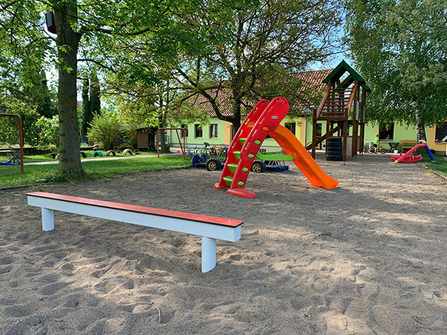 Leerer Spielplatz mit Sandkasten, Bank, Rutsche und vielen grünen Bäumen