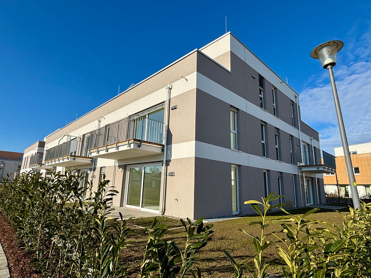 Seitliche Ansicht eines Neubau MEhrfamilienhauses mit weiß-beiger Farbe. Es sind Balkone zu sehen.