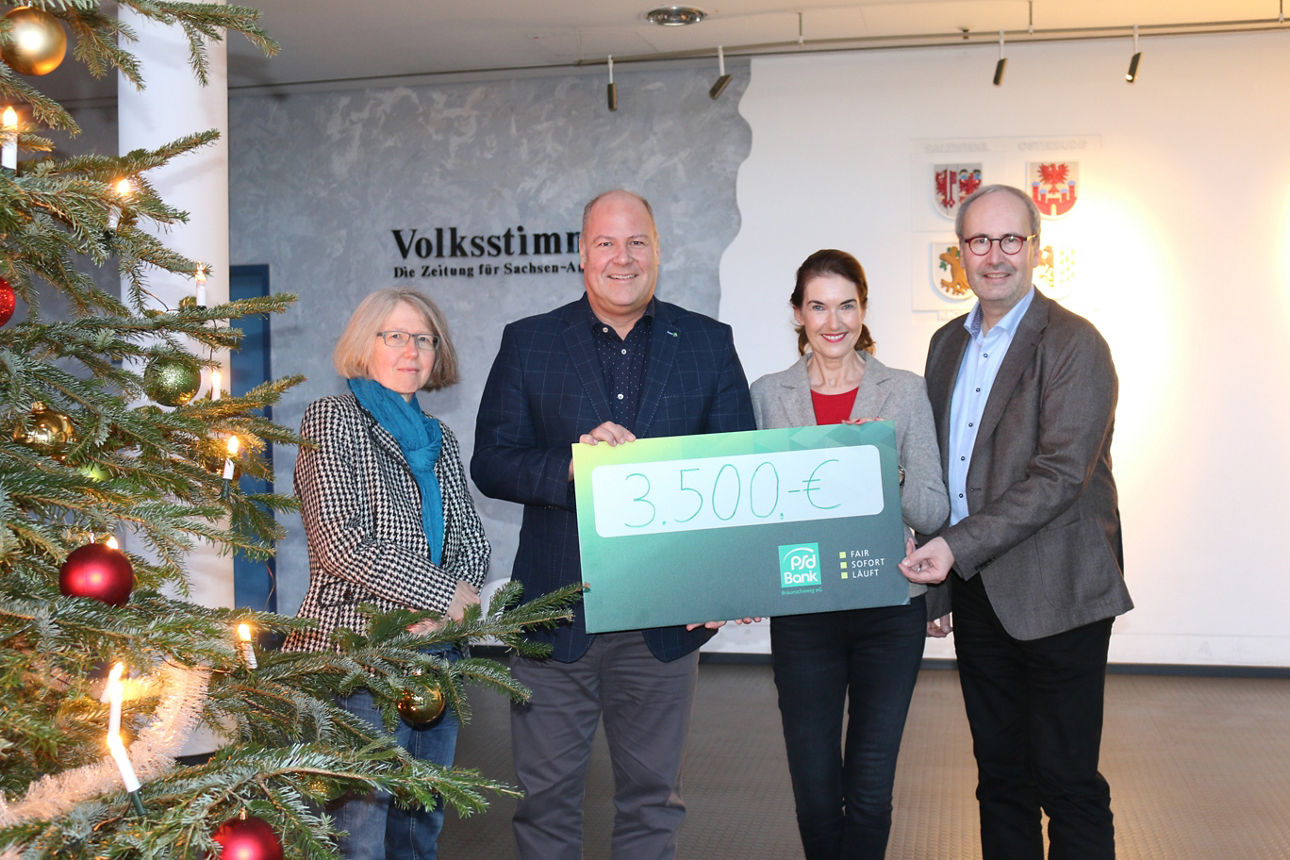 Vier Menschen halten einen Scheck neben einem Weihnachtsbaum