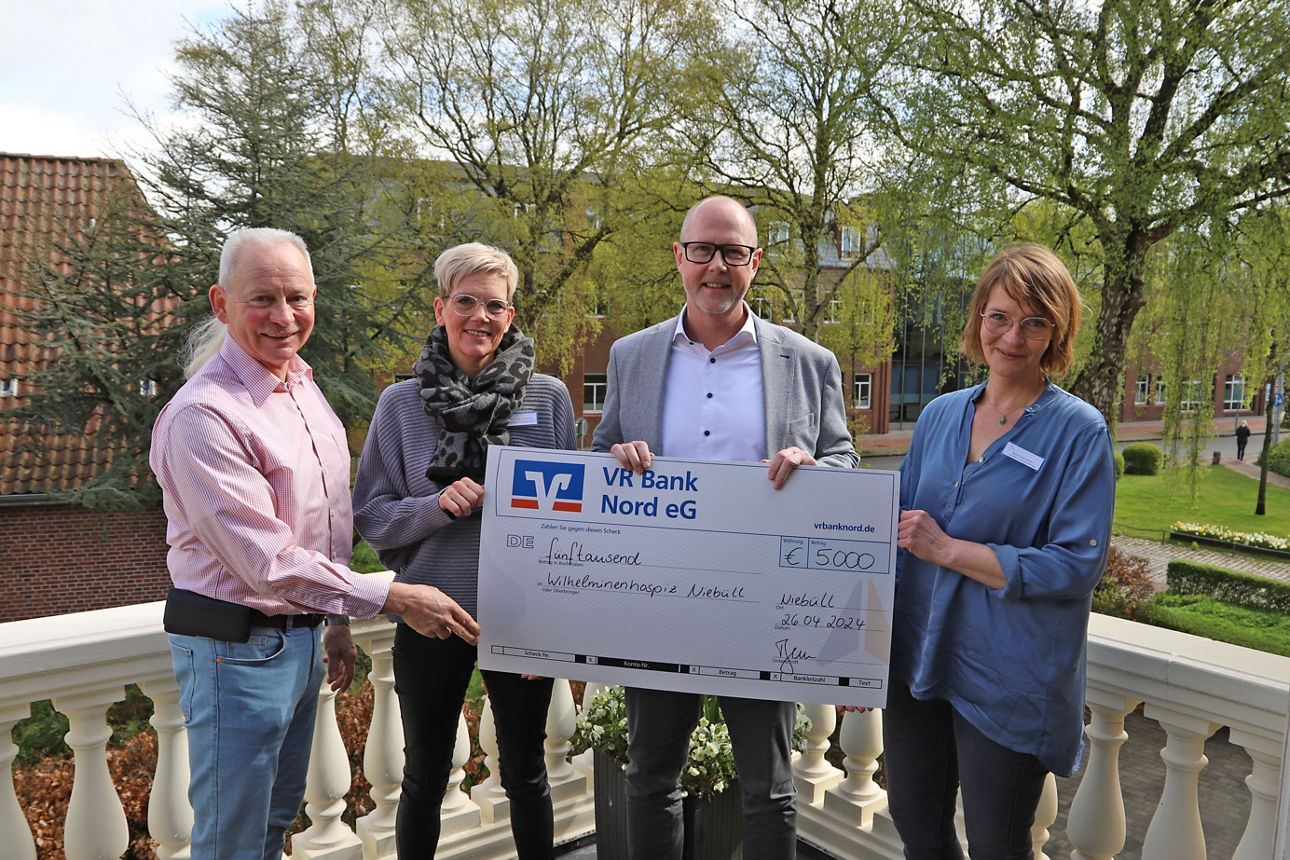 Vier lächelnde Menschen halten einen großen Spendenscheck in den Händen