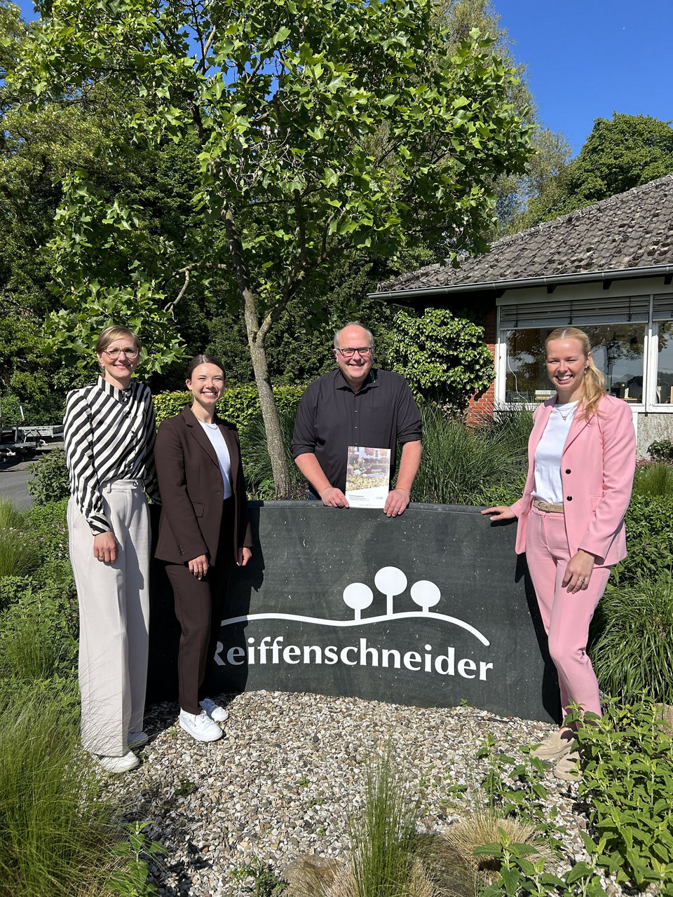 Vier Personen vor Firmenschild, ein ESG‑Bericht wird gezeigt.