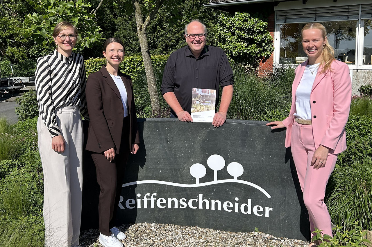 Vier Personen vor Firmenschild, ein ESG‑Bericht wird gezeigt.