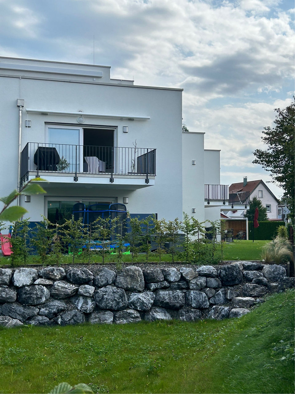 Garten eines Neubau Mehrfamilienhauses mit Blick auf einen Balkon.