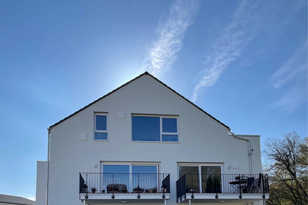 Neubau eines weißen Mehrfamilienhauses von der seitlichen Ansicht mit Balkonen.