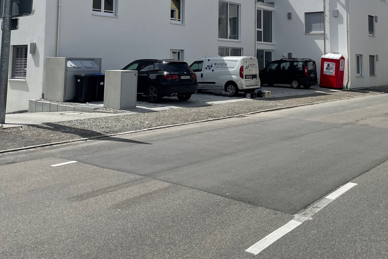 Weißes neues Mehrfamilienhaus mit Spitzdach in Wangen im Allgäu. Es sind Parkplätze zu sehen.