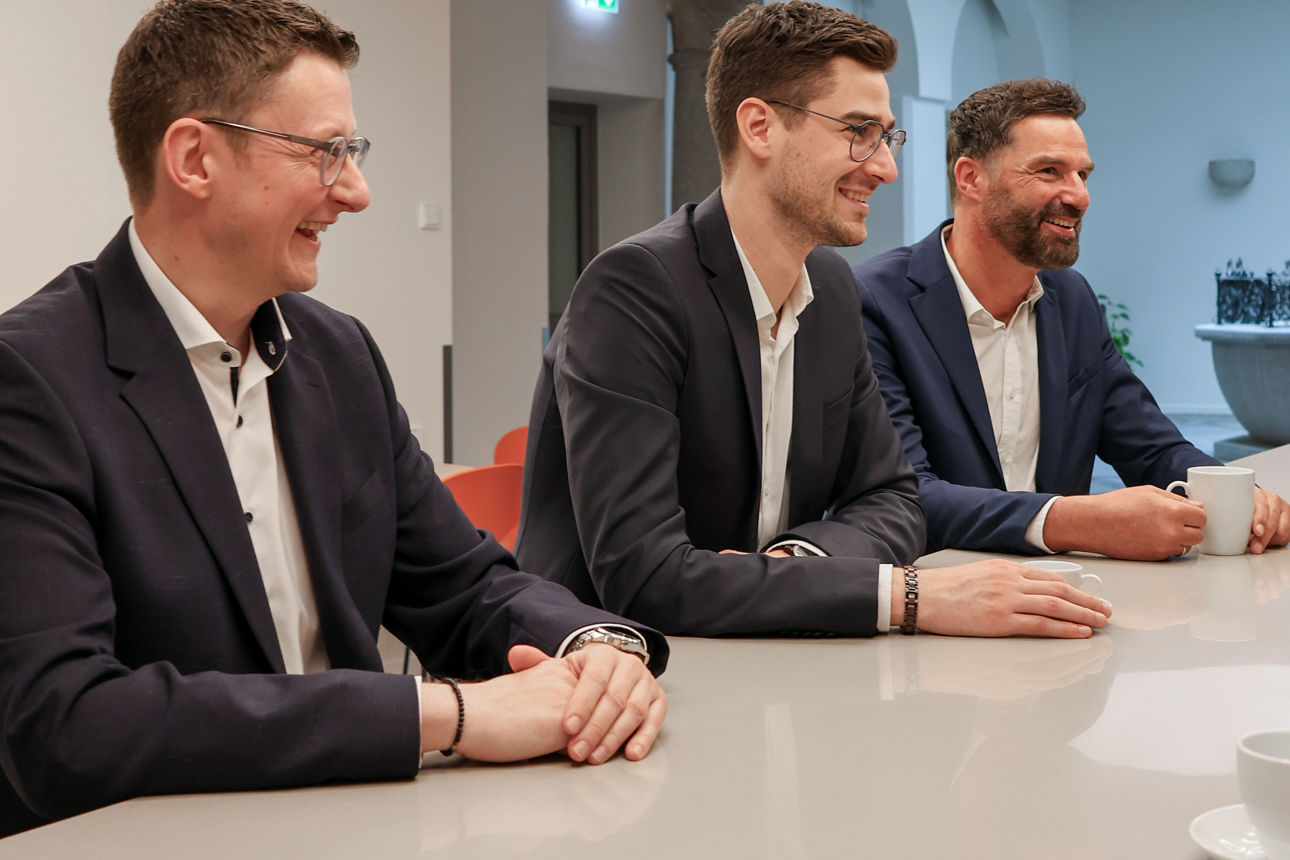 Drei Männer sitzen gemeinsam am Tisch und lachen