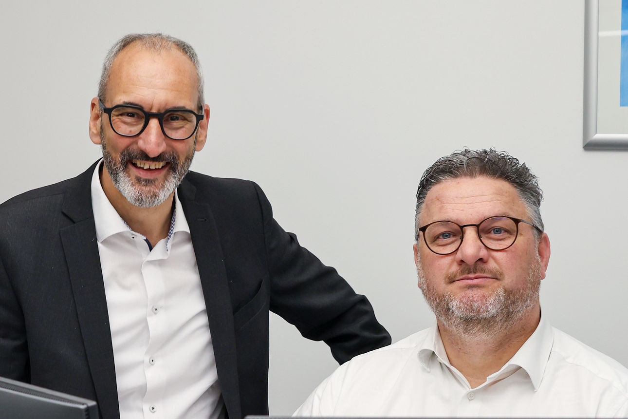Zwei Männer sitzen vorm PC und lächeln
