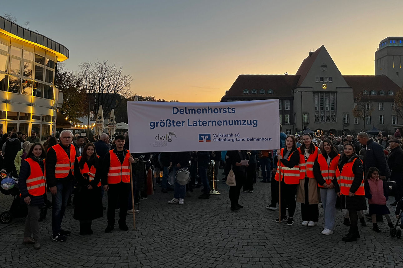 Menschen halten ein Banner hoch mit der Aufschrift "Delmenhorsts größter Laternenumzug"