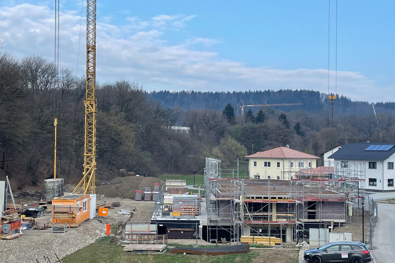 Rohbau eines Neubau Mehrfamilienhauses mit Baugerüsten aus der Fernsicht. Außenrum ist LAndschaft mit Bäumen zu sehen.