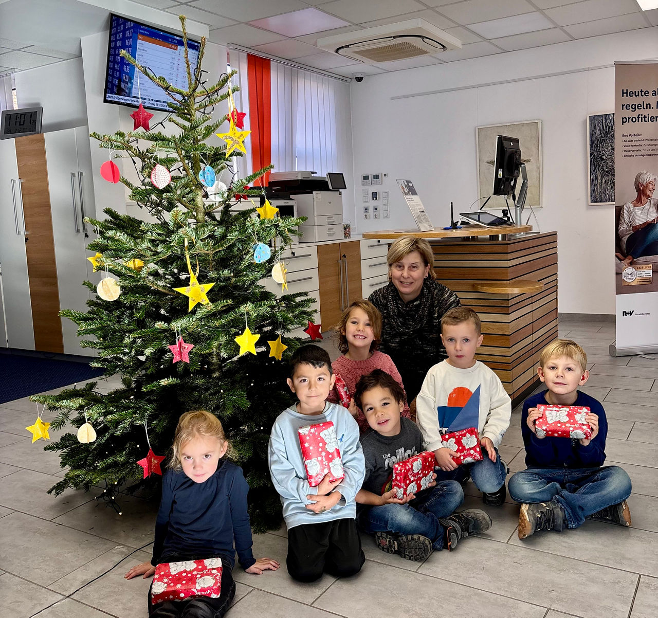 Kinder in der Bankfiliale mit Geschenken und einem Weihnachtsbaum. 