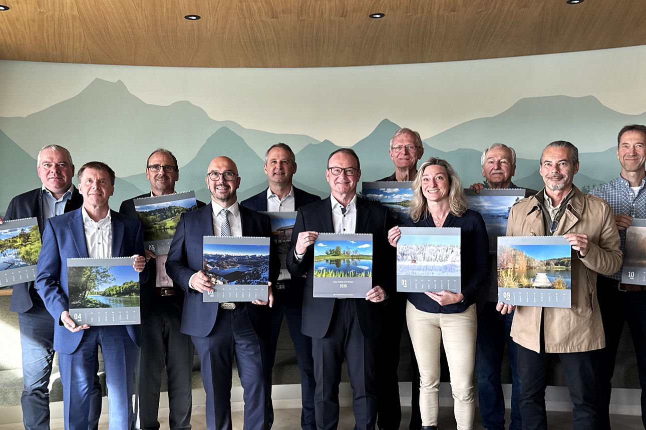 Gruppe mit 11 Personen, davon eine Frau, alle halten den neuen Fotobildkalender 2026 in den Händen, jeweils mit einem anderen Motiv, 