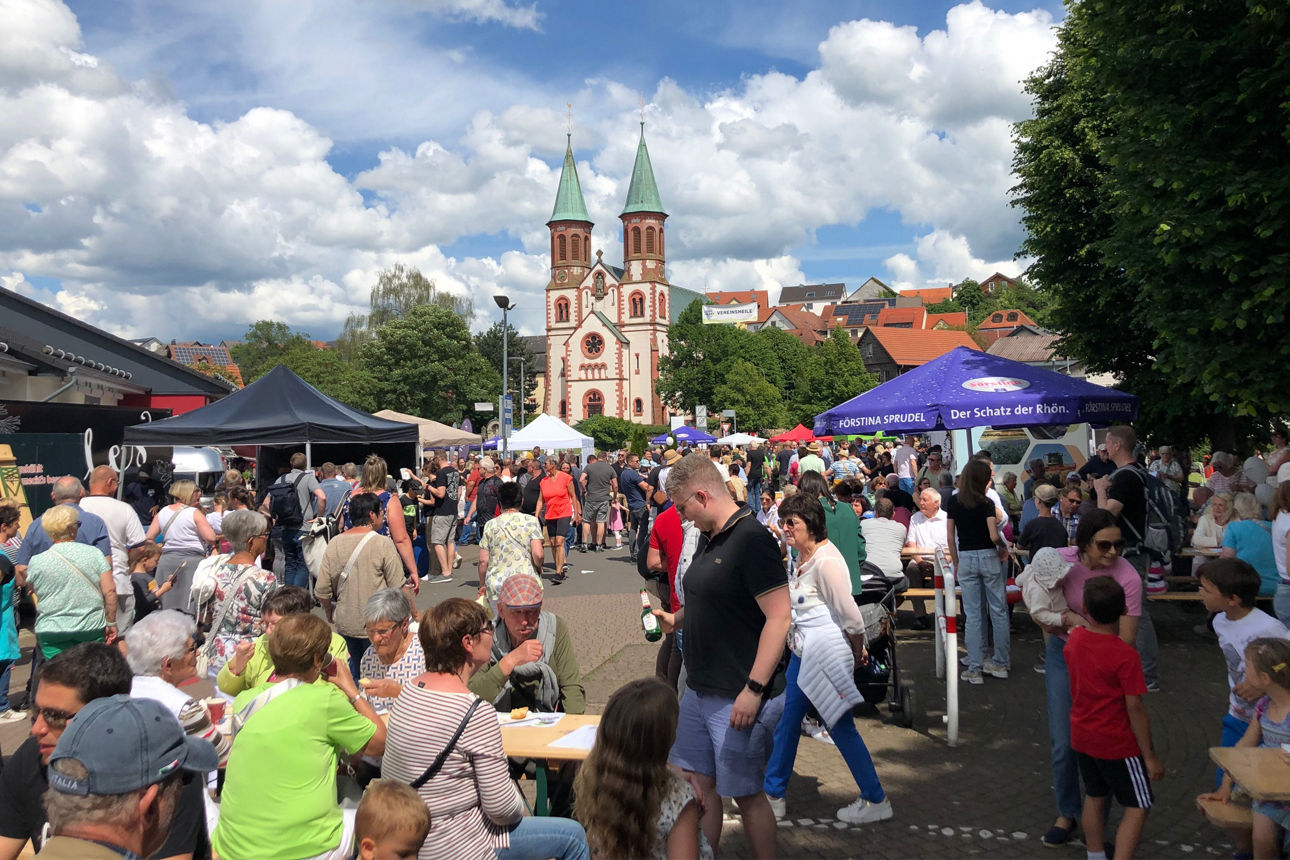 Belebter Marktplatz mit Menschen und Ständen, Kirche im Hintergrund bei Stadtfest