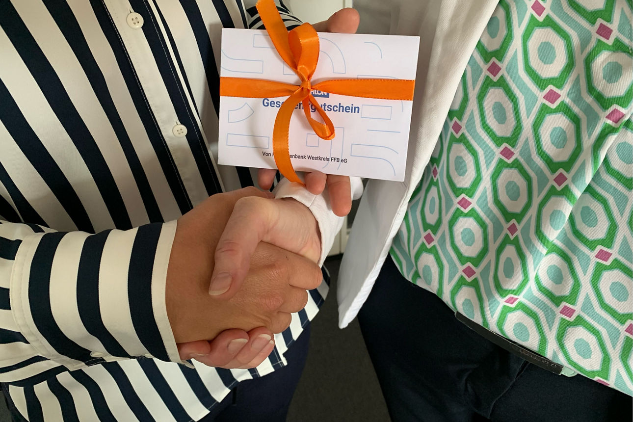 Zwei Mitarbeitende geben sich die Hand und halten einen Geschenkgutschein.