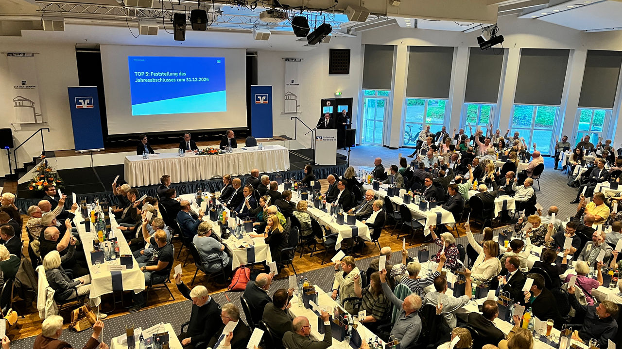 Saal mit vielen Menschen und einer Präsentation auf einer Leinwand im Hintergrund