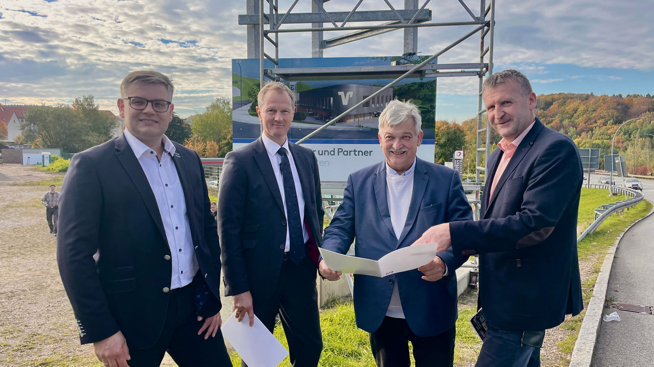 4 Männer stehen vor der Baustelle mit dem Bauplan