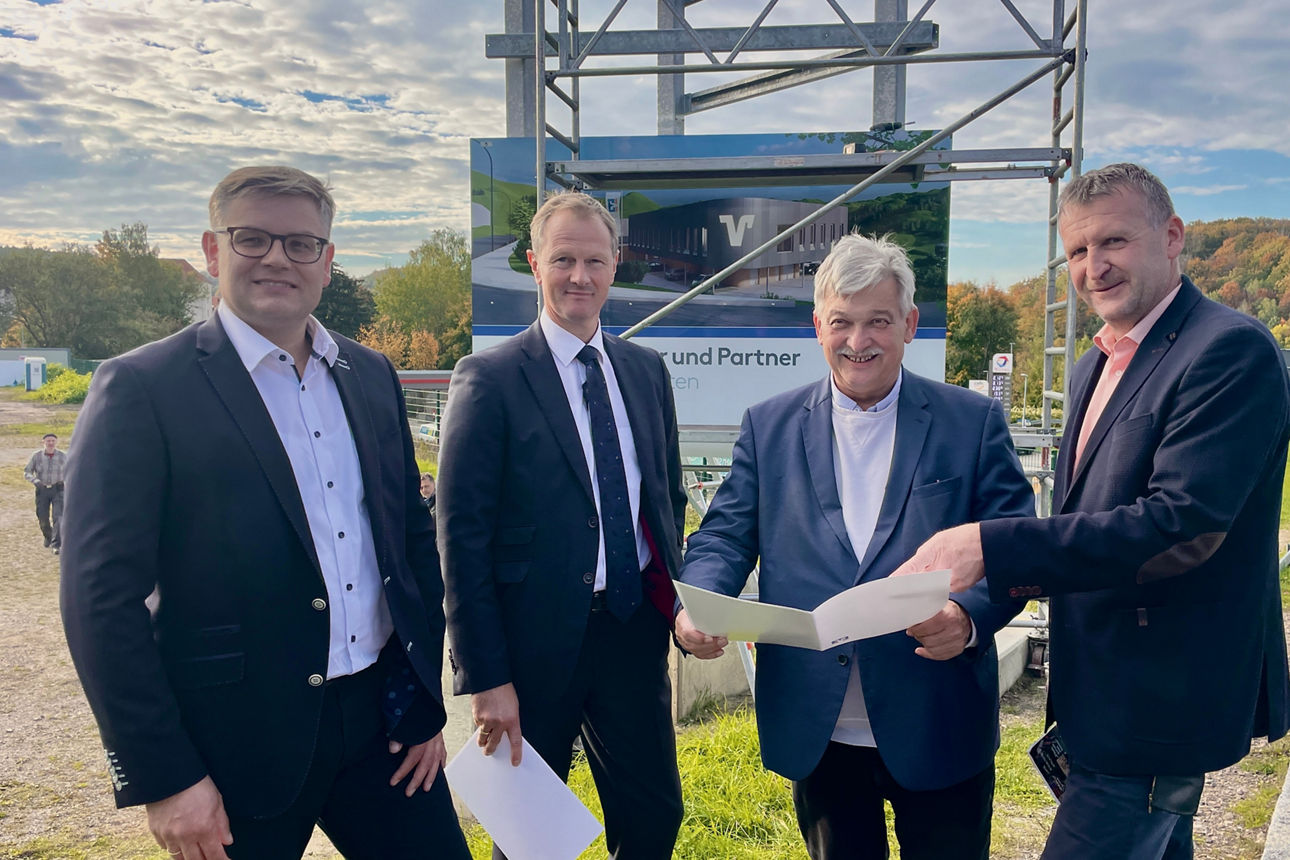 4 Männer stehen vor der Baustelle mit dem Bauplan