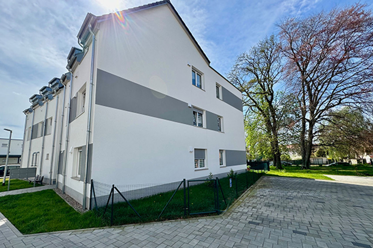 Voller Wohnblock mit Dach von der Seite gesehen und mit Bäumen und Grünfläche auf der Rückseite