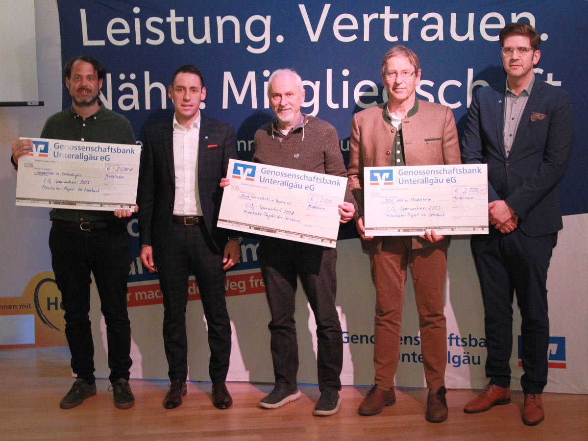 Mitgliedes des Vereins stehen mit großen Spendenschecks nebeneinander vor einer Leinwand
