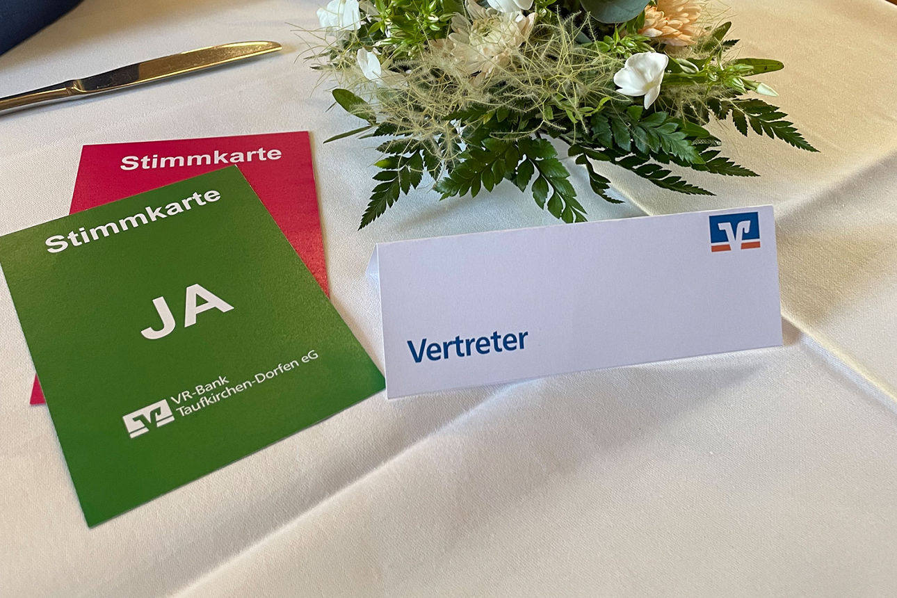 blumige Tischdekoration auf weißer Tischdecke und Abstimmungskarten in grün und rot zu sehen.