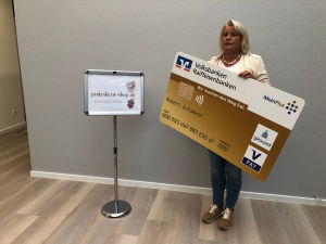 eine blonde, weiß gekleidete Frau, die einen Preis hält