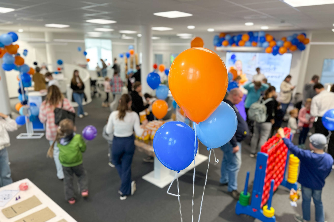 Mehrere orangefarbene und blaue Luftballons in einem Raum mit vielen Menschen und Spielgeräten.