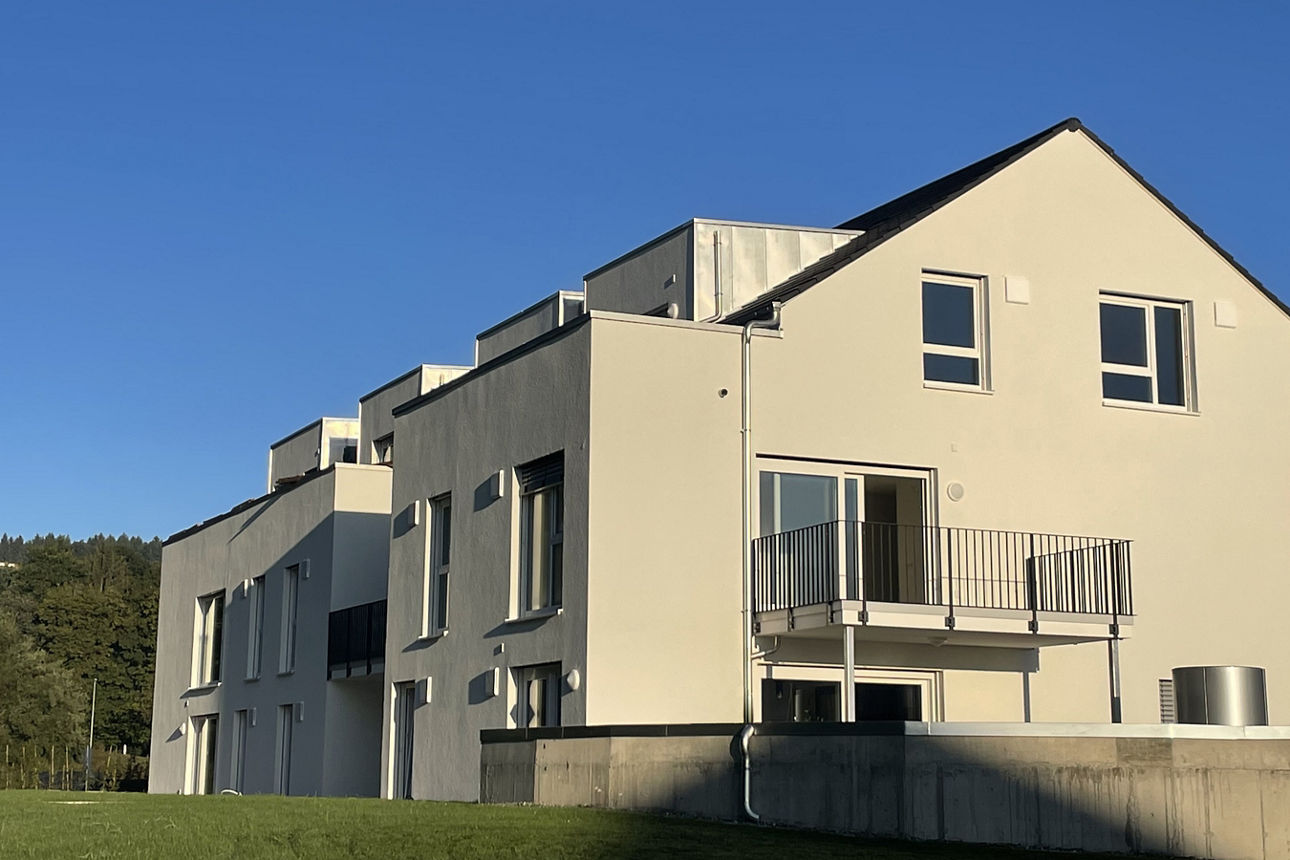 Neubau eines weißen Mehrfamilienhauses von der seitlichen Ansicht mit Balkonen bei untergehender Sonne.