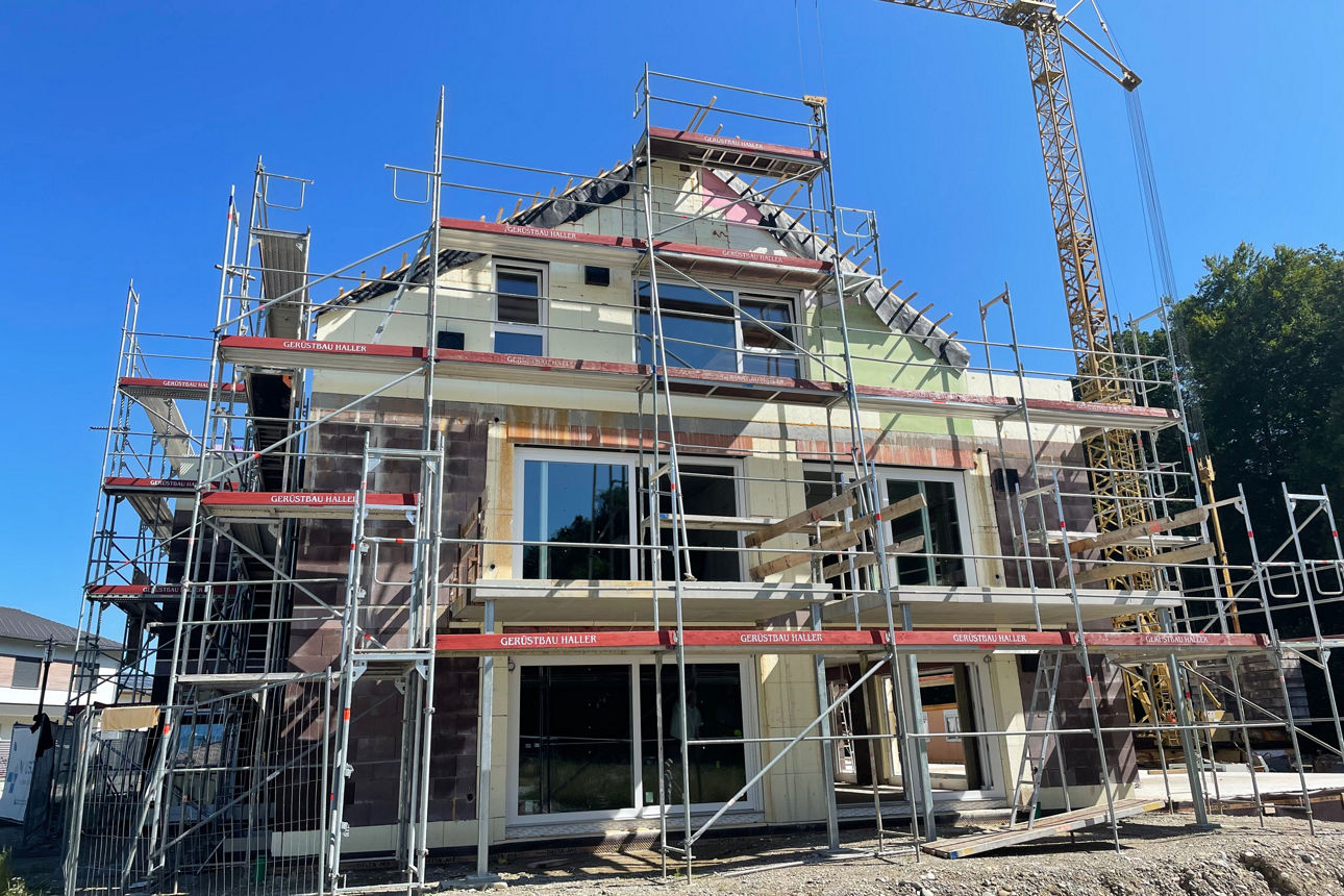 Rohbau eines Neubau Mehrfamilienhauses mit Baugerüsten. Daneben ein Kran.