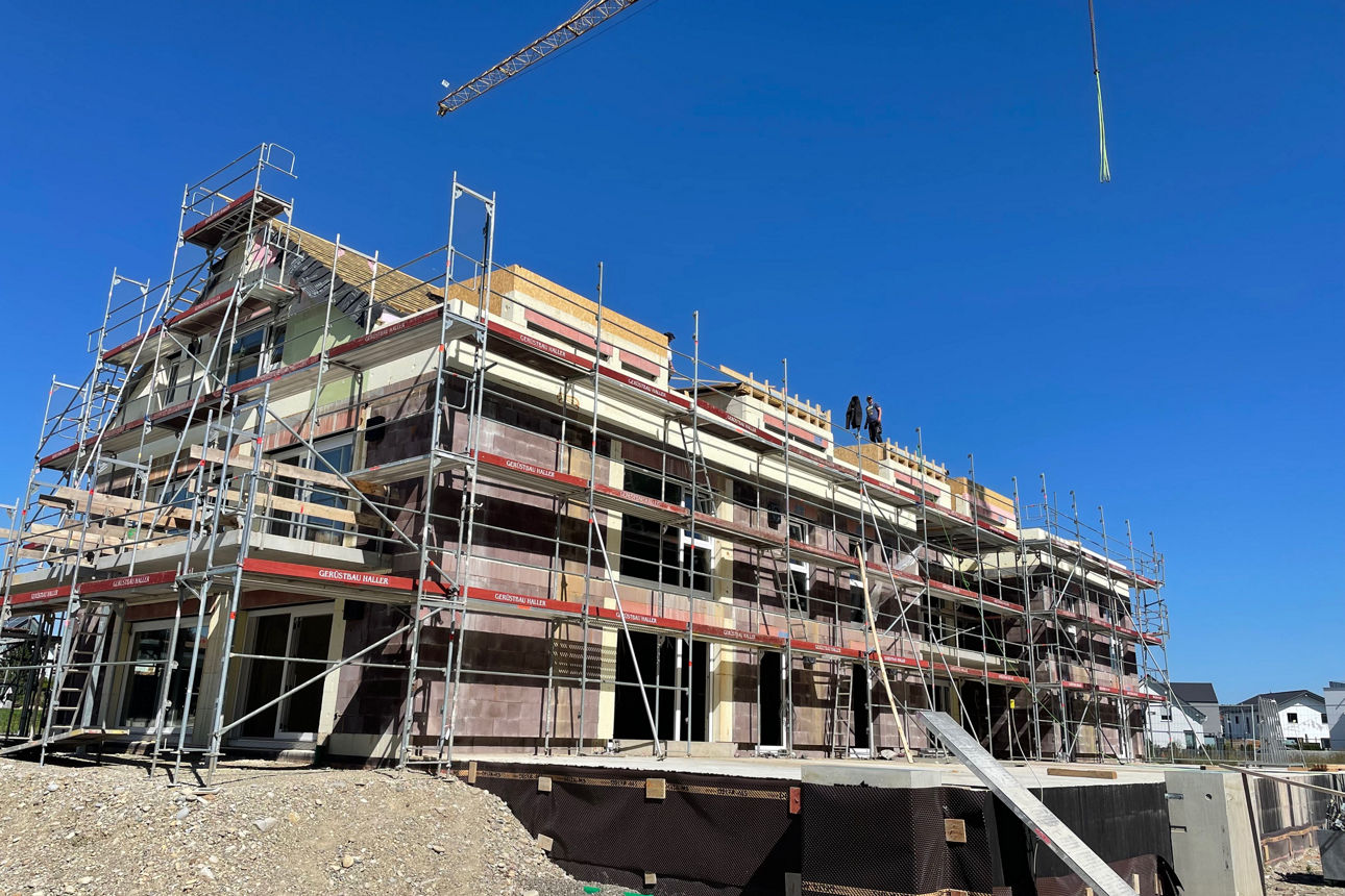 Rohbau eines Neubau Mehrfamilienhauses mit Baugerüsten vor blauem Himmel.