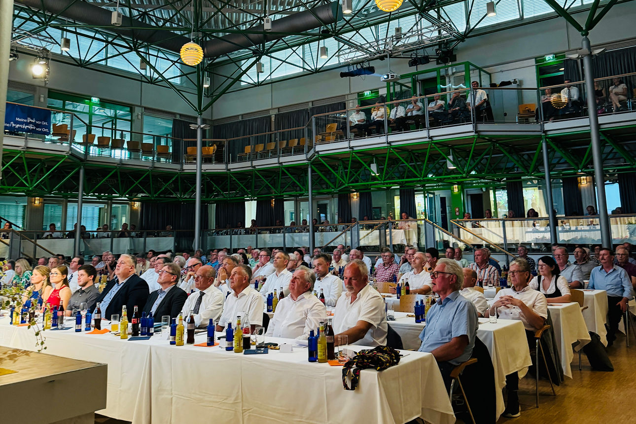 Großer Saal mit vielen Personen an Tischen bei einer Versammlung