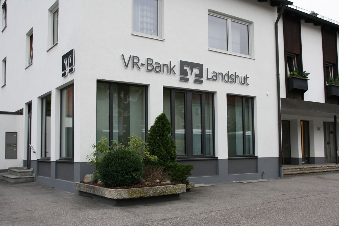 Ein weißes Gebäude an einer Hauptstraße mit wenigen Parkplätzen vor der Tür