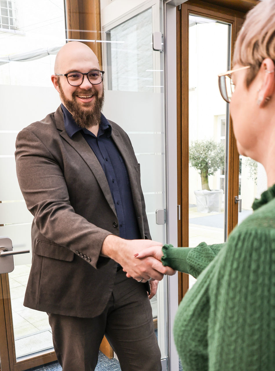 Eine lachende Dame mit einer Tasse Kaffe in der Hand, ein lachender Herr mit einer Flasche Wasser in der Hand