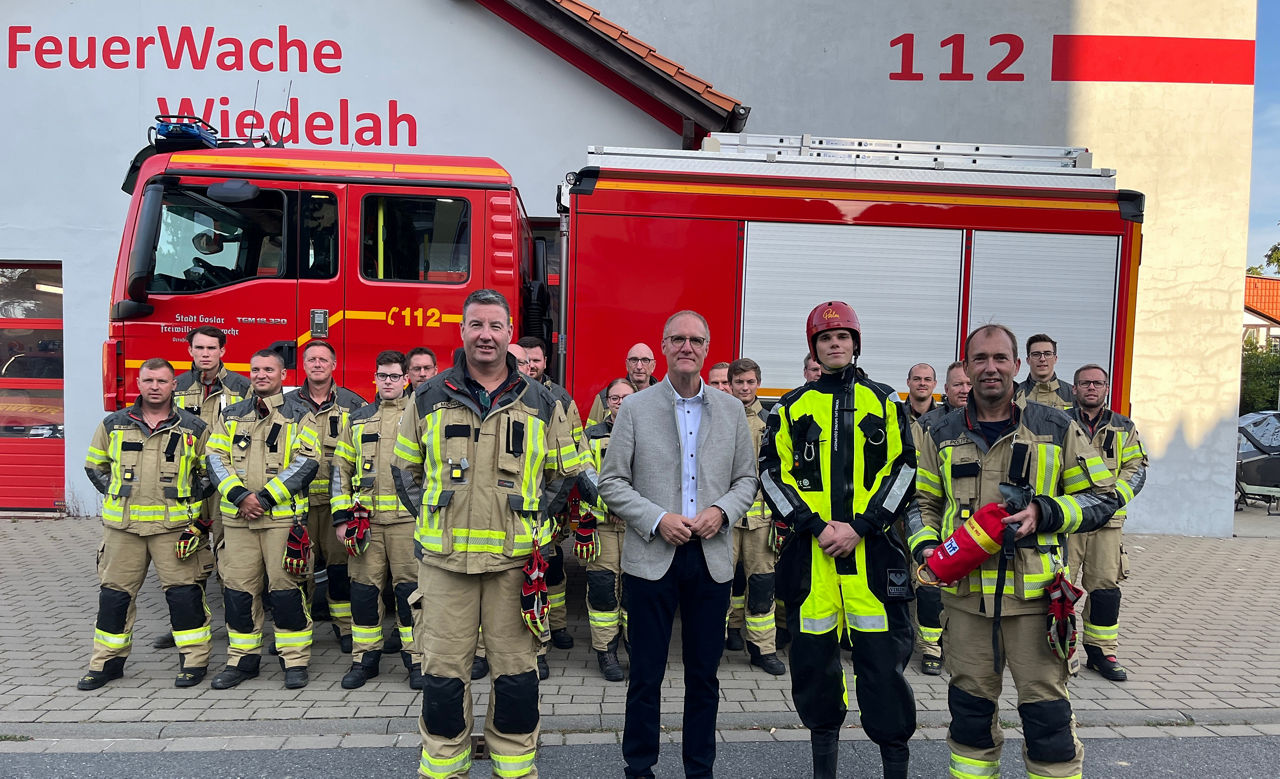 Eine Gruppe von Feuerwehrleuten und unserem Vorstand vor einem Feuerwehrauto vor der Wache in Wiedelah.