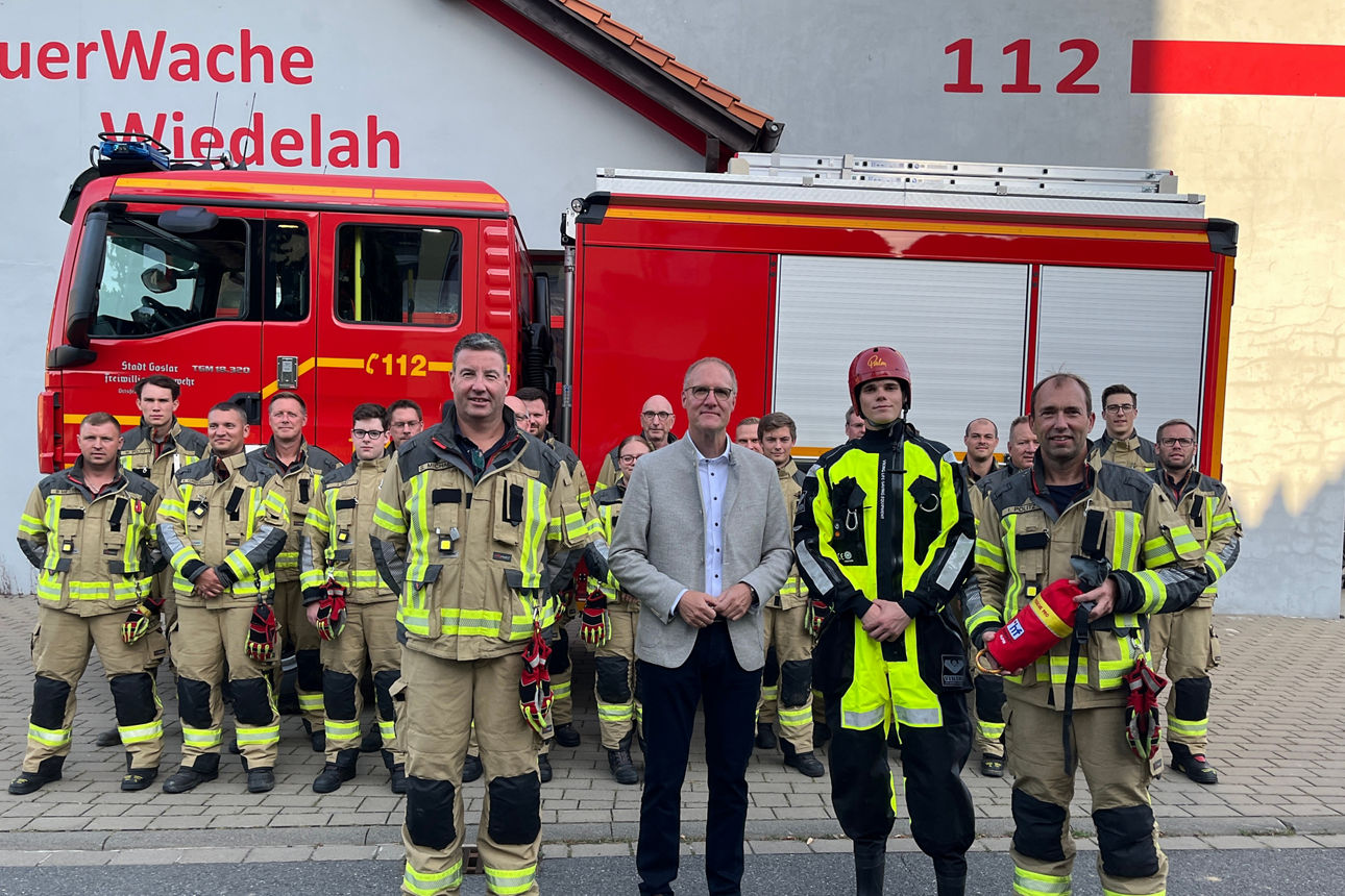 Eine Gruppe von Feuerwehrleuten und unser Vorstand vor einem Feuerwehrauto vor der Wache in Wiedelah