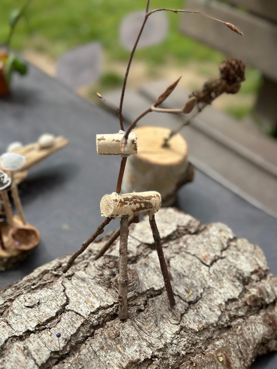 Kleine Figur aus Ästen und Kork auf Baumrinde, die ein Tier darstellt