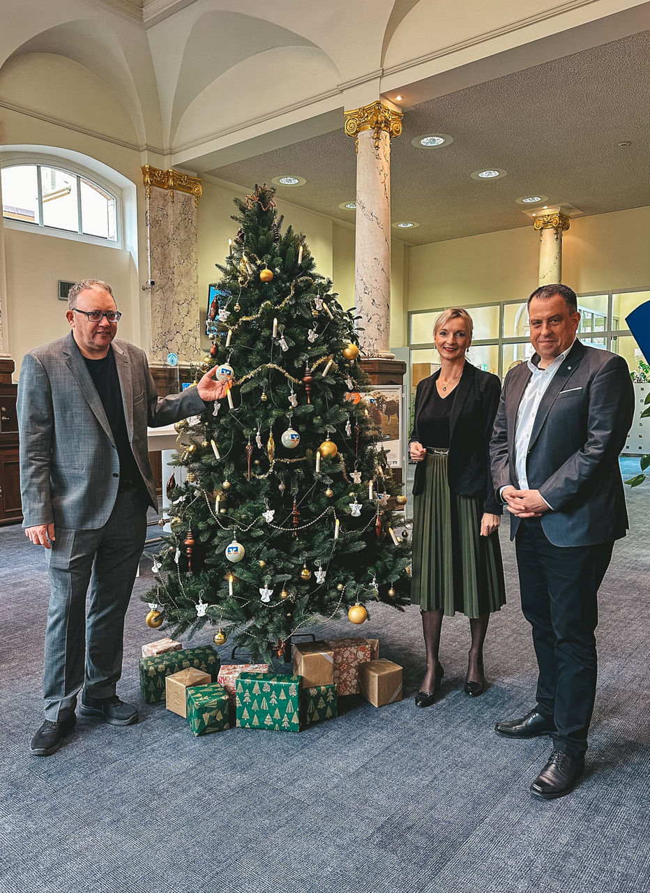 Drei Personen, zwei Männer und eine Frau, in der Nähe eines Weihnachtsbaums