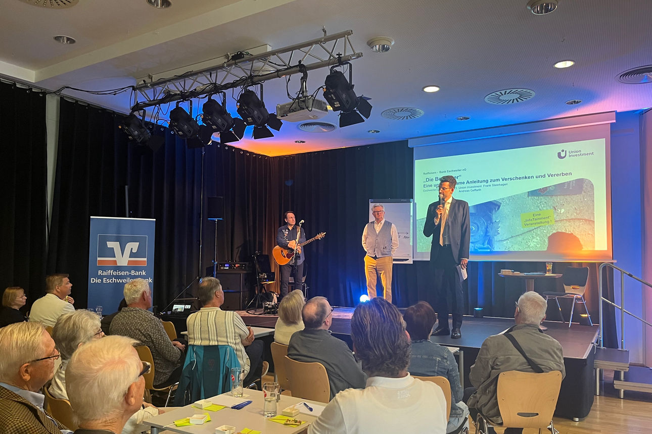 Eine Bühne mit einem Herren der einen Vortrag hält und Zuschauer. 