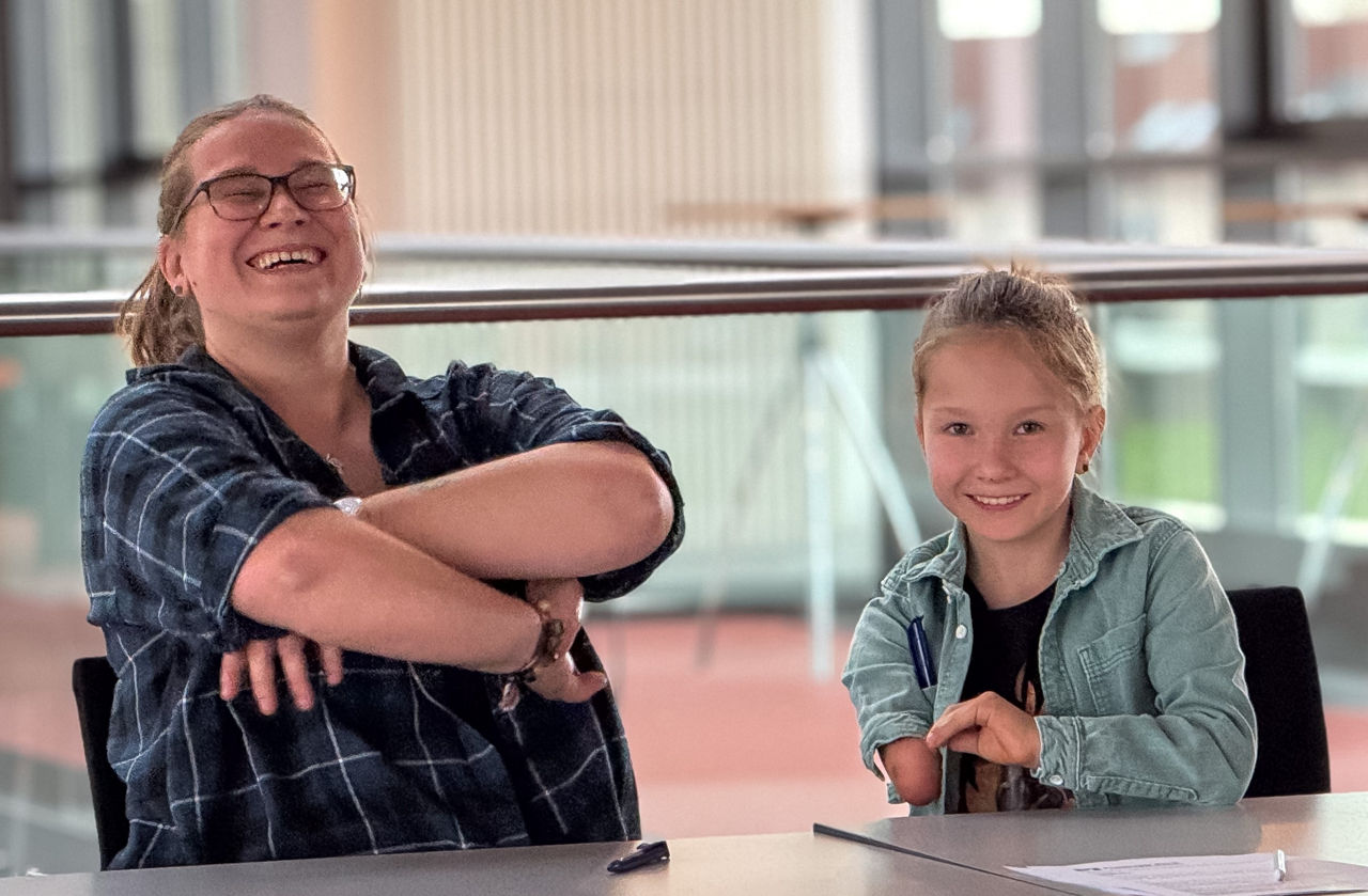 Mutter und kleiner Sohn sitzen lachend an Tisch mit Blick in einen modernen hellen Raum; hinter ihnen ein Geländer aus Glas