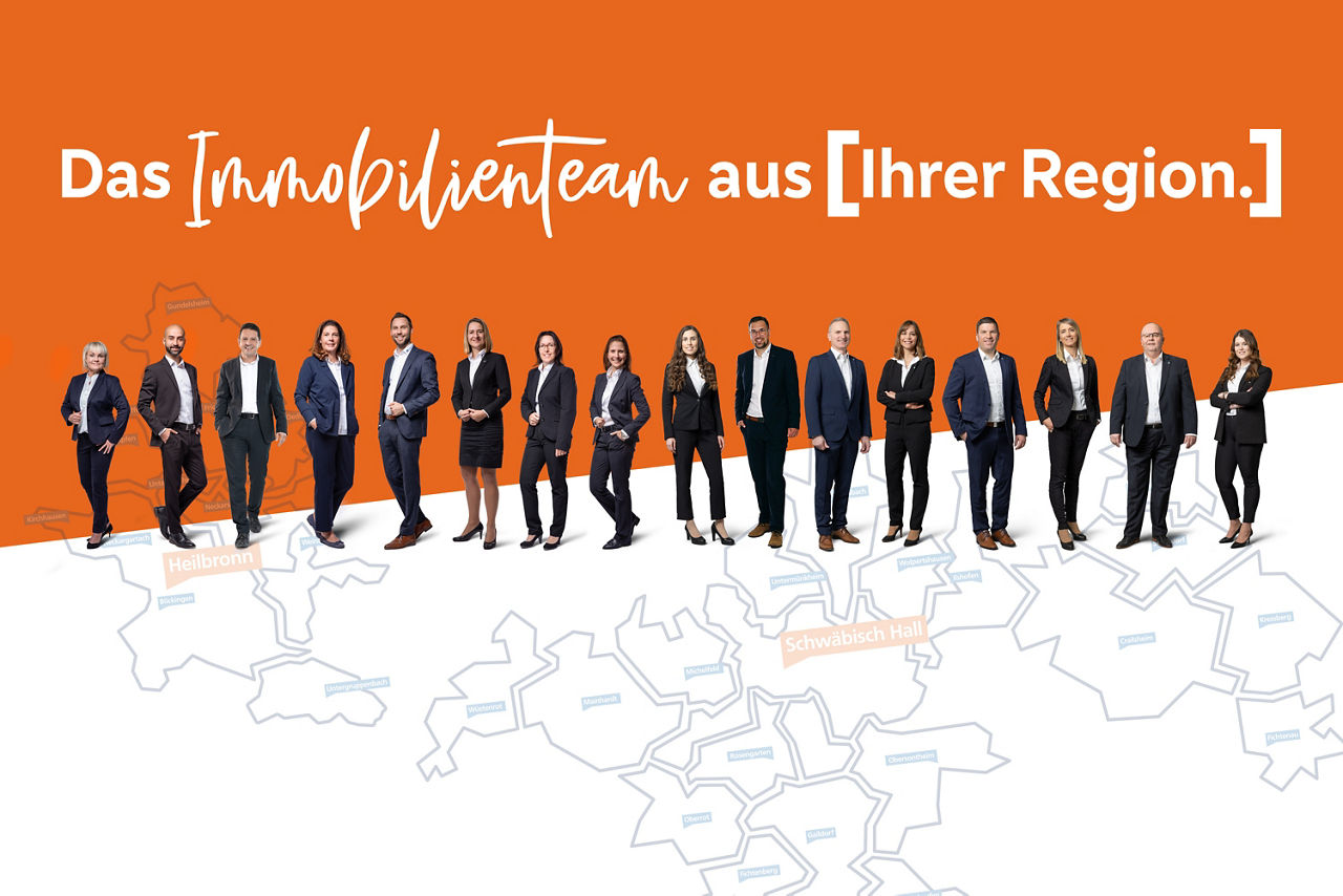 Das Team der Immobilienabteilungen stehen nebeneinander aufgereiht vor einem orangefarbenen Hintergrund mit der Aufschrift „Das Immobilienteam aus Ihrer Region.“. 