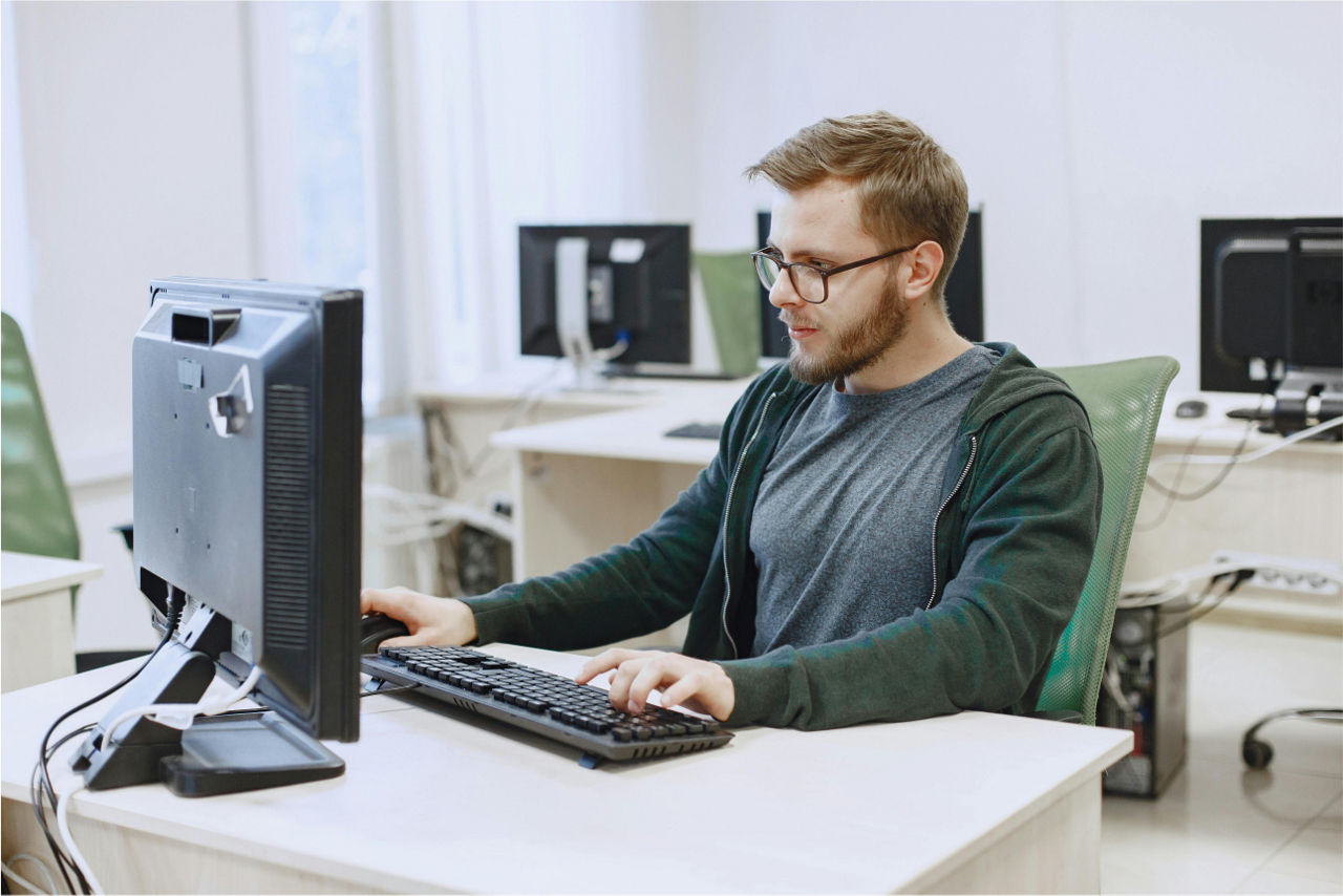 Ein Mann sitzt an einem Tisch vor einem PC und tippt auf einer Tastatur. 