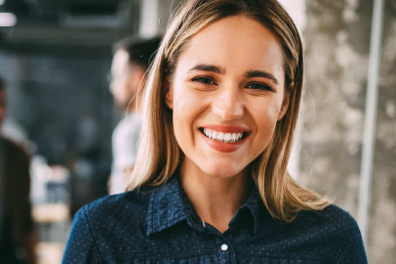Eine Dame lächelt und im Hintergrund sind zwei Kollegen zu erkennen