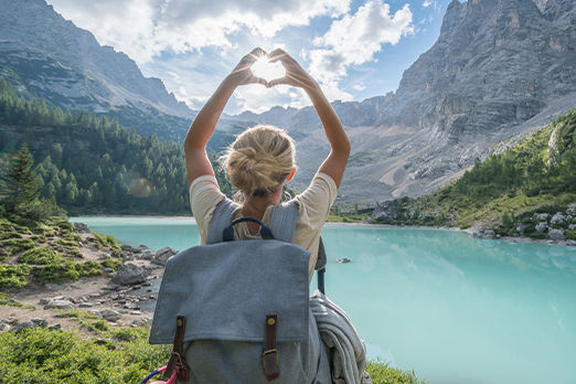 junge Frau mit Rucksack steht vor Berglandschaft