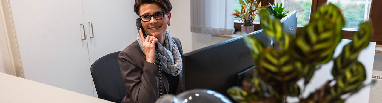Telefonierende Frau sitzt lächelnd im Büro 