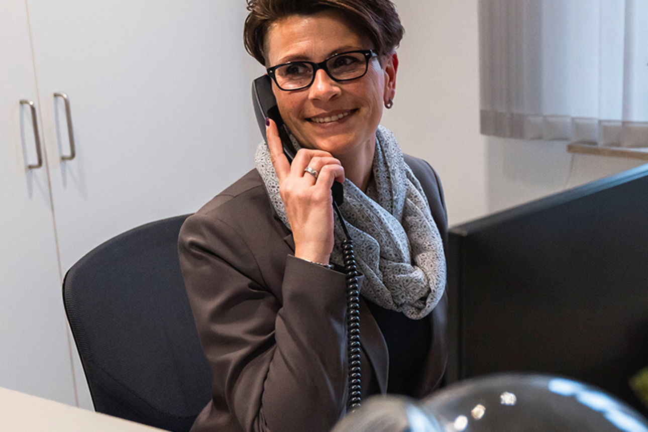 Telefonierende Frau sitzt lächelnd im Büro 