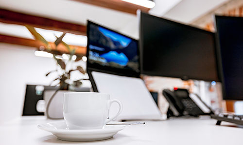 Tisch mit Tasse und Monitoren in einem Büroraum