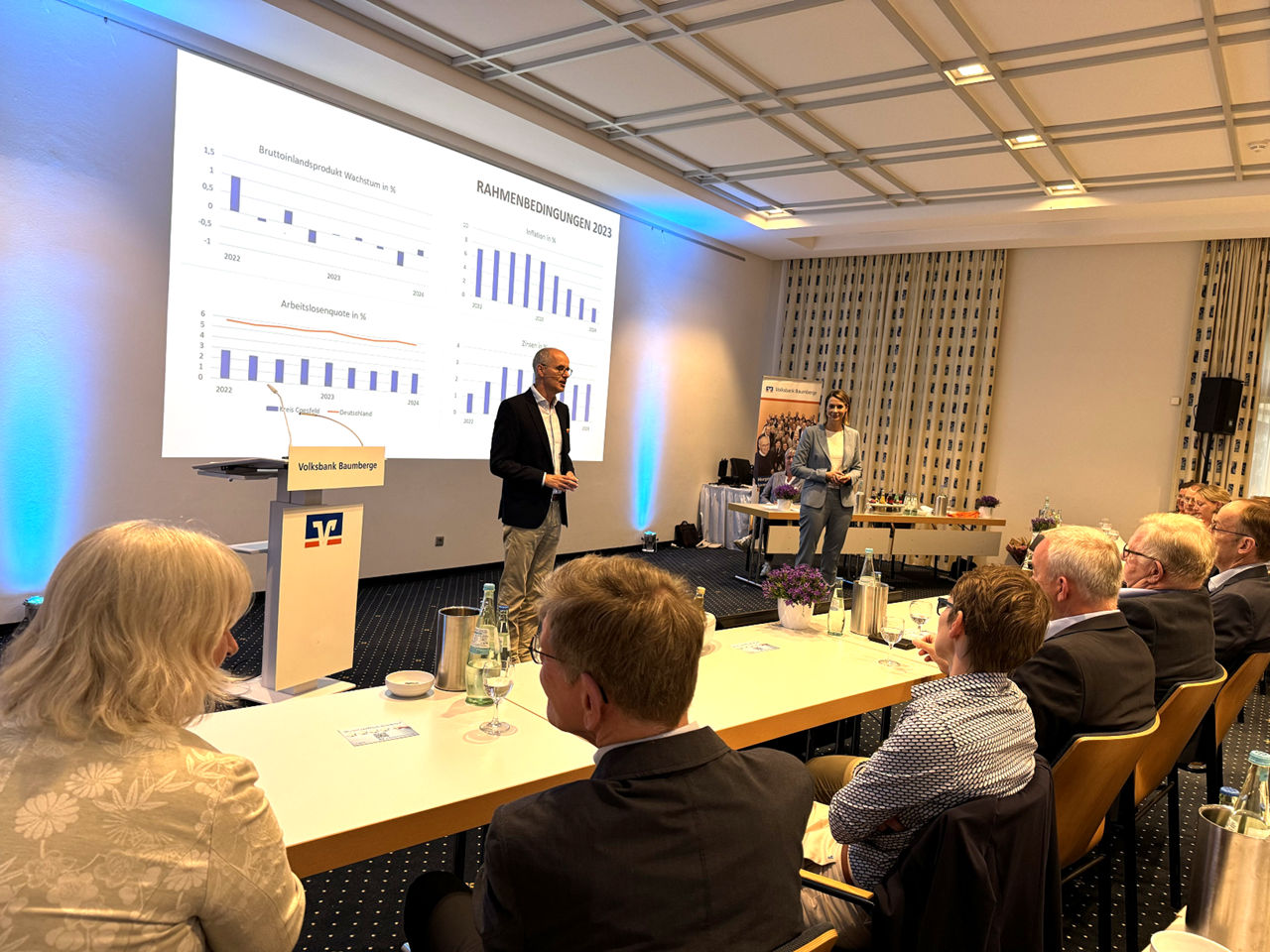 Ein Mann steht an einem Podium in einem Konferenzraum und hält einen Vortrag vor einer Gruppe von sitzenden Zuhörern