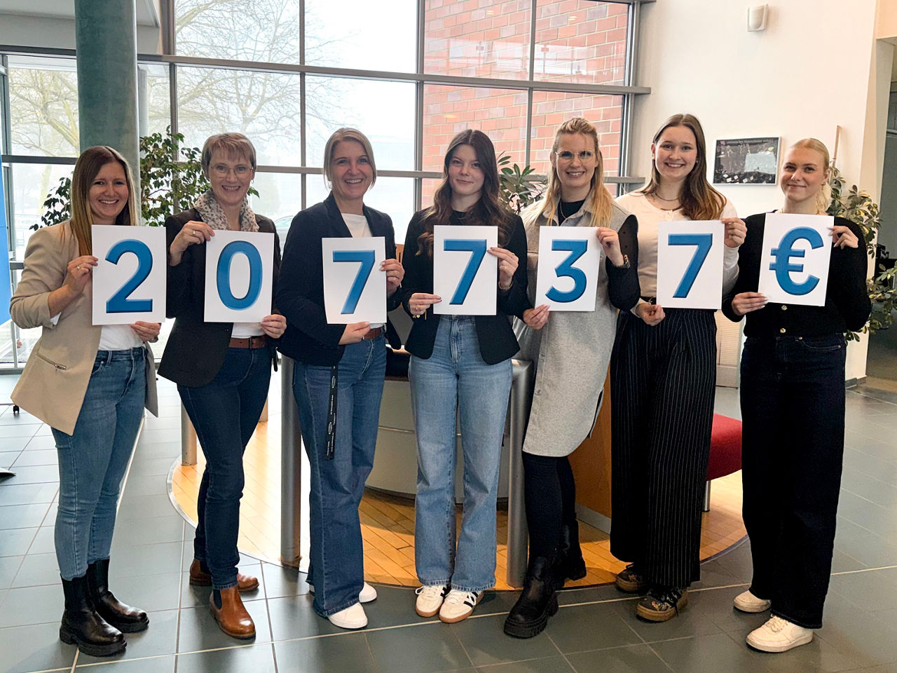 Sieben Frauen halten Schilder mit „20.773,17 €“ in hellem Raum, gemeinsames Spendenfoto