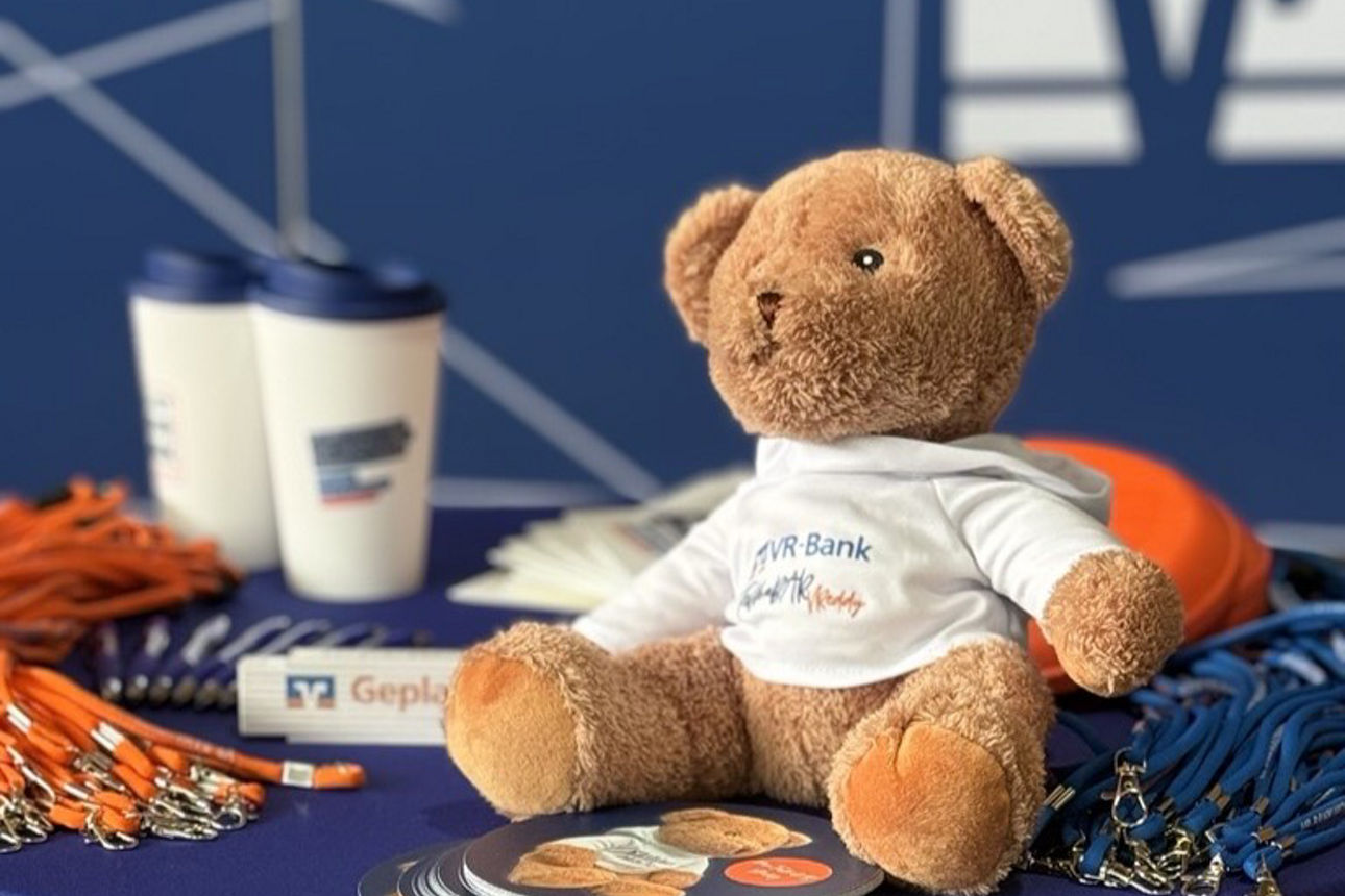 Teddybär sitzt auf einem Stehtisch zwischen Werbemitteln