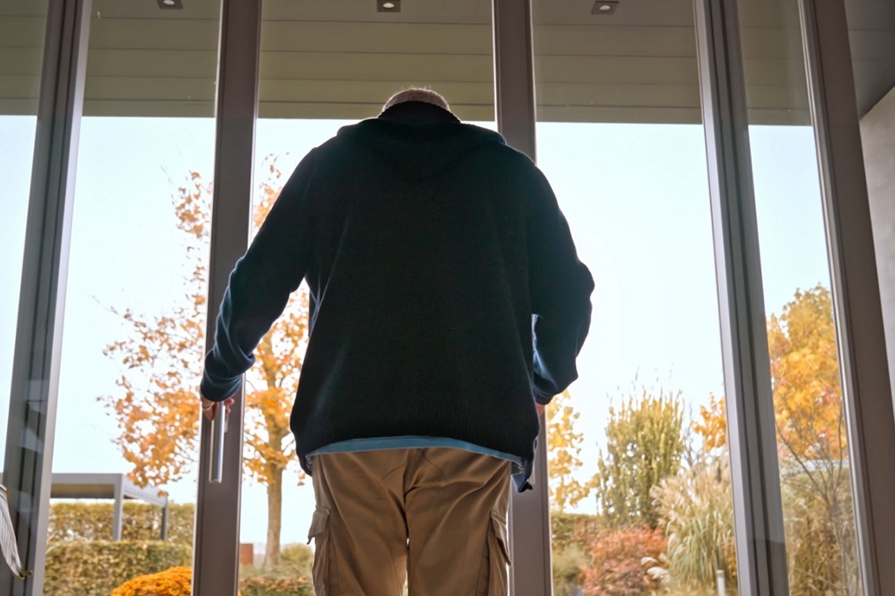 Ein Mann steht mit dem Rücken zur Kamera und öffnet die Terassentür in seinen Garten.